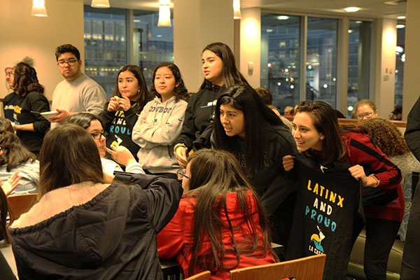 A group of young students gathered around a table with one holding a "Latinx and Proud" t-shirt