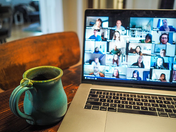 A laptop with a Zoom interface on the screen next to a green mug on a wooden table